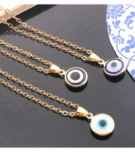 Detailed view of three gold evil eye necklaces in blue, white, and light blue on black surface