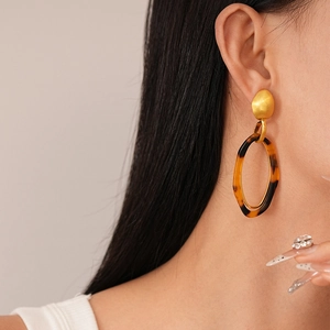 Detail view of oval leopard print resin earrings worn by a model in soft beige light