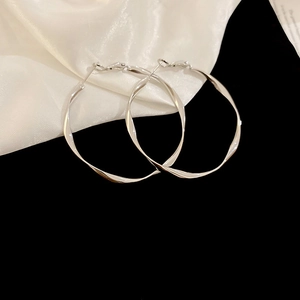 Detail of large silver hoop earrings with twisted metal texture on white silk fabric