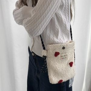 Close-up of white plush crossbody bag featuring red heart patch and rope strap detail