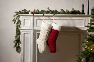 Close-up of cable knit Christmas stockings with heart tassels hanging on a fireplace mantel