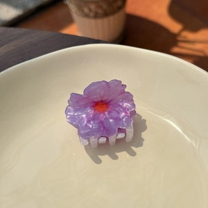 Close-up of a purple acetate flower hair claw clip on an elegant ceramic plate
