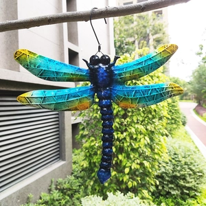 Detailed close-up of a blue metal dragonfly wall decor hanging on a garden branch