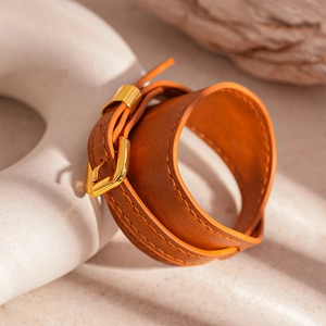 Close-up of brown faux leather double wrap bracelet with gold buckle on a white sculpture