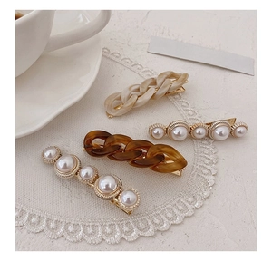 Detail of four elegant hair clips featuring resin chains and pearls on white lace