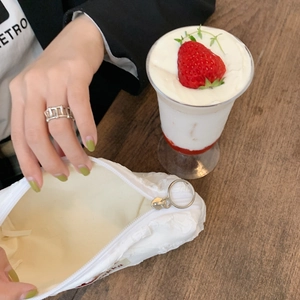 White puffy floral pouch with ring zipper pull on a wooden table with a strawberry drink