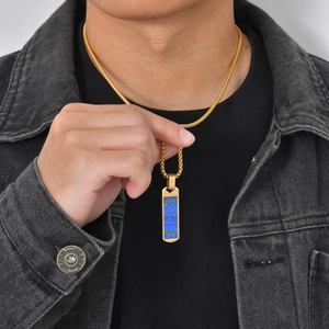 Close-up of men's gold necklace with blue lapis lazuli pendant worn by model on denim