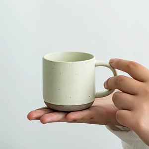 Speckled light green ceramic espresso cup with a brown stoneware base in hand