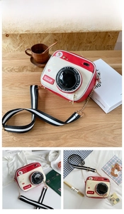 Detail of red and cream camera-style crossbody bag with striped strap on wood