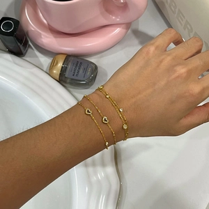 Close-up of triple layered gold 18k bracelets with heart and round charms on wrist