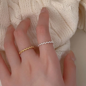 Close-up of minimalist silver and gold beaded rings worn on fingers over a knit sweater