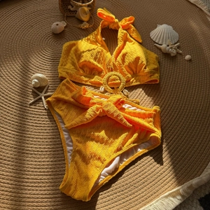 Macro shot of textured yellow swimwear fabric featuring shell charms and ring detail