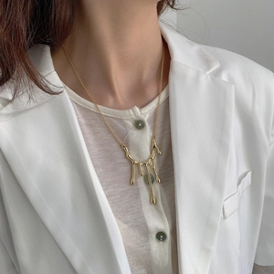 Close-up of a gold lava textured pendant necklace worn by a model in a white blazer