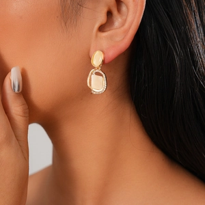 Detail of gold-tone earrings with cream stones and rhinestones worn by a model