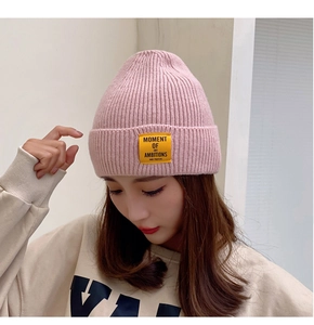 Detailed close-up of a pink knitted beanie with a yellow lettered patch on the front side