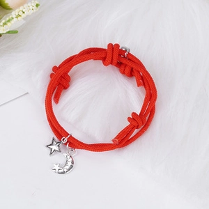 Detail of red woven bracelet with silver moon and star charms on white faux fur