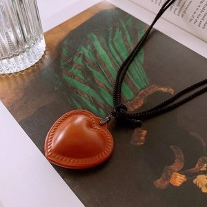 Close-up of heart-shaped faux leather pendant necklace on an artistic book page