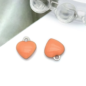 Detailed view of two orange enamel heart pendants with polished metal rims and loops