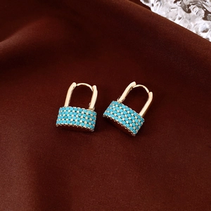 Close-up of golden lock-shaped earrings with inlaid turquoise beads on brown silk