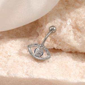 Silver evil eye navel ring with blue gem on rustic stone surface and white silk