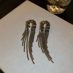 Close-up of gold tassel earrings with black rhinestones on a textured display box