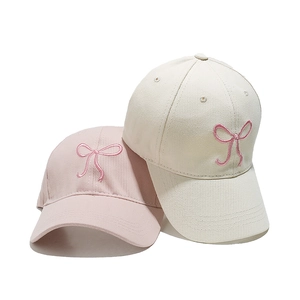 Close-up of pink and beige baseball caps featuring delicate embroidered ribbon bows