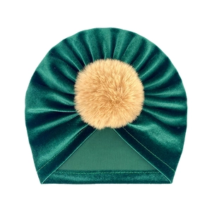 Detail of baby velvet beanie in emerald green featuring a soft brown faux fur pompom