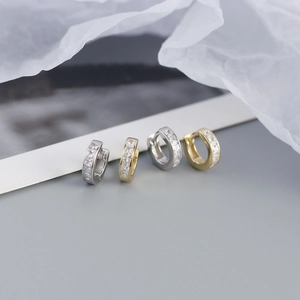 Detailed close-up of gold and silver square-cut zircon huggie earrings on grey surface