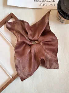 Macro detail of large bronze satin bow scrunchie on wooden frame with coffee cup
