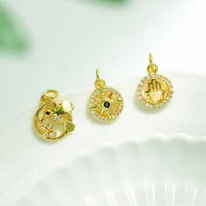 Macro detail of 18K gold plated hummingbird, compass and Hamsa hand charm pendants