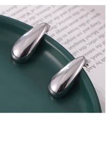 Close-up of teardrop-shaped silver-tone earrings with polished finish on ceramic plate
