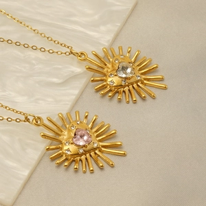 Détail du pendentif cœur soleil doré avec zircone rose sur un fond en marbre