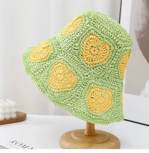 Detail of hand-crocheted green straw hat with yellow heart patterns on a wooden stand