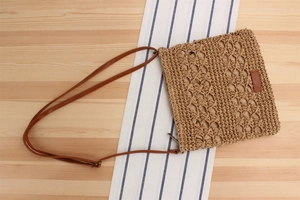 Detailed texture of brown straw crossbody bag on a striped cloth over wooden background