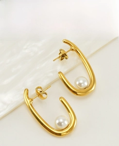 Detail of U-shaped gold earrings with white pearls on a rippled background board