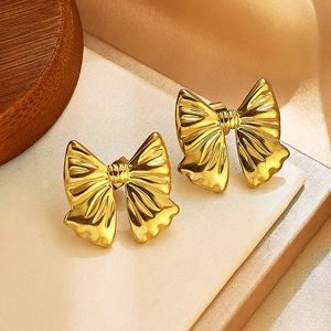 Gros plan de boucles d'oreilles nœuds plaquées or avec texture sur tissu crème