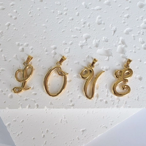 Pendentifs alphabet LOVE en acier inoxydable doré 18K sur fond avec gouttes d'eau