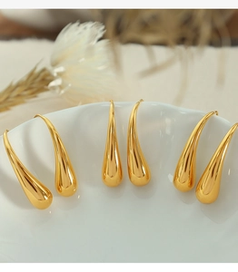 Macro shot of elegant gold teardrop earrings on a white ceramic dish with soft lighting