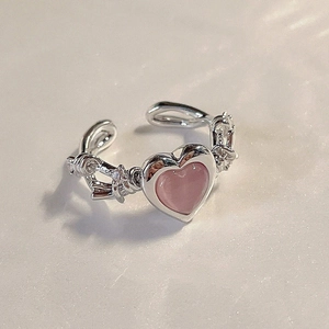 Macro detail of silver heart ring with pink stone and zircon bow on marble background