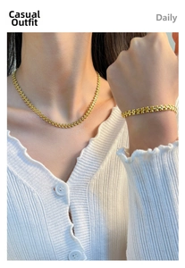 Close-up of a gold-plated flower link necklace and bracelet set worn on a white cardigan
