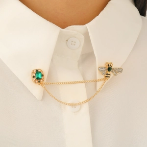 Detail of bee brooch with emerald cut green gemstone and golden double chains