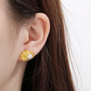 Detailed close-up of golden irregular textured earrings with pearl inlays worn by a model