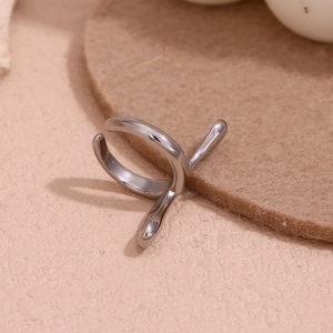Close-up of minimalist silver stainless steel cross ear cuff on a textured background