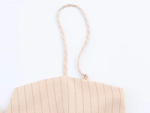 Détail rapproché de la texture du tissu rayé beige et des fines bretelles du haut