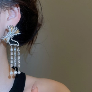 Macro detail of silver tassel earrings with zircon bow and pearls on a female model