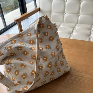 Detailed close-up of yellow flower embroidery on beige canvas tote bag with simple wish tag