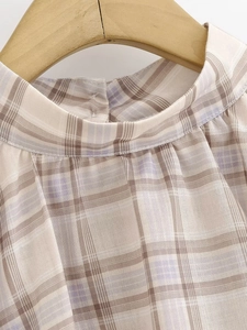 Macro view of plaid blouse neckline featuring pleated details and soft beige fabric