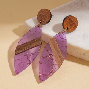 Detailed shot of bohemian leaf earrings with purple resin, wood texture, and gold foil