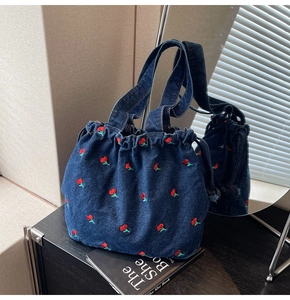 Detail view of denim bucket bag featuring vibrant cherry embroidery and drawstring closure