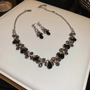 Elegant waterdrop necklace and earring set with black and clear crystals on white texture